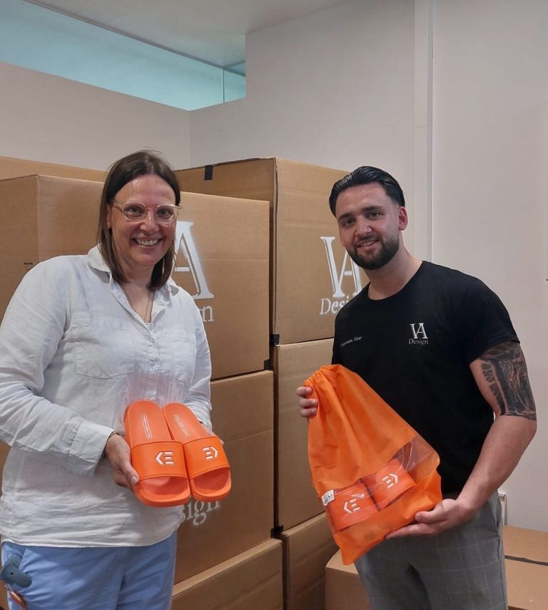 Übergabe Klinikum Esslingen Zwei Personen halten orangefarbene Taschen vor einem Stapel von Kartons.