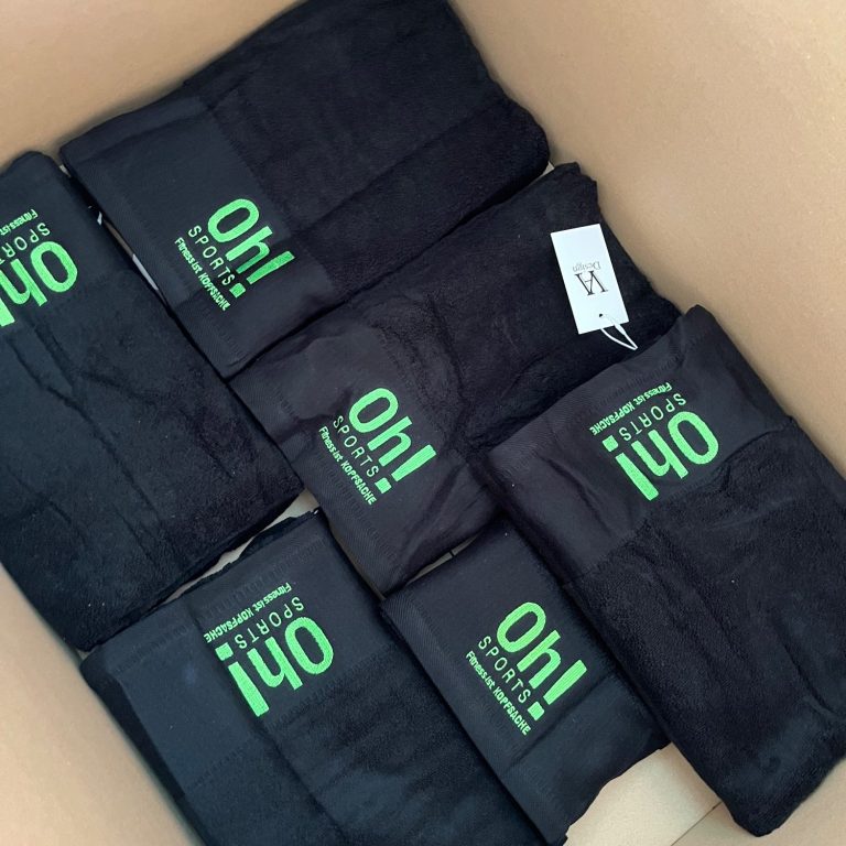 Gym Angebot Schwarze Tücher mit grüner "Oh!"-Aufschrift in einem Karton.